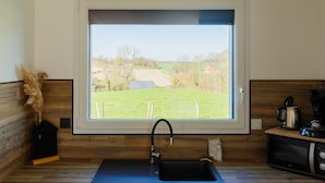 A kitchen with a window, a sink, a microwave, and a small house-shaped object on the left. - Gîte 'Le Nid Des Prés' with Private Terrace and Garden (Val-de-Scie)
