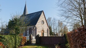 A church with a pointed steeple, brick walls, and a circular window. - Gîte 'Le Nid Des Prés' with Private Terrace and Garden (Val-de-Scie)