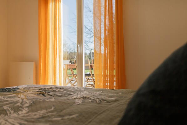 A room with a bed, a window with orange curtains, and a view of the outdoors. - Gîte 'Le Nid Des Prés' with Private Terrace and Garden (Val-de-Scie)