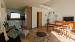 A modern living room with a sofa, chairs, a dining table, and a TV. - Gîte 'Le Nid Des Prés' with Private Terrace and Garden (Val-de-Scie)