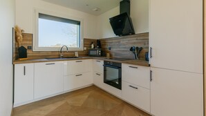 A modern kitchen with white cabinetry, a microwave, an oven, and a window providing natural light. - Gîte 'Le Nid Des Prés' with Private Terrace and Garden (Val-de-Scie)
