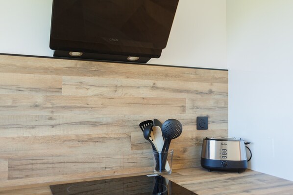 A kitchen with a toaster, a glass container with utensils, and a wooden backsplash. - Gîte 'Le Nid Des Prés' with Private Terrace and Garden (Val-de-Scie)