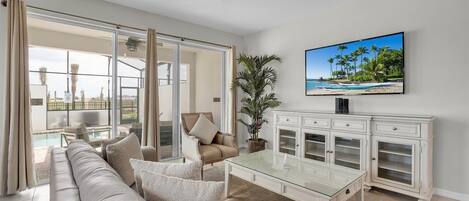 Un salón amplio con una mesa de centro de vidrio, un sofá color beige y un televisor montado en la pared.