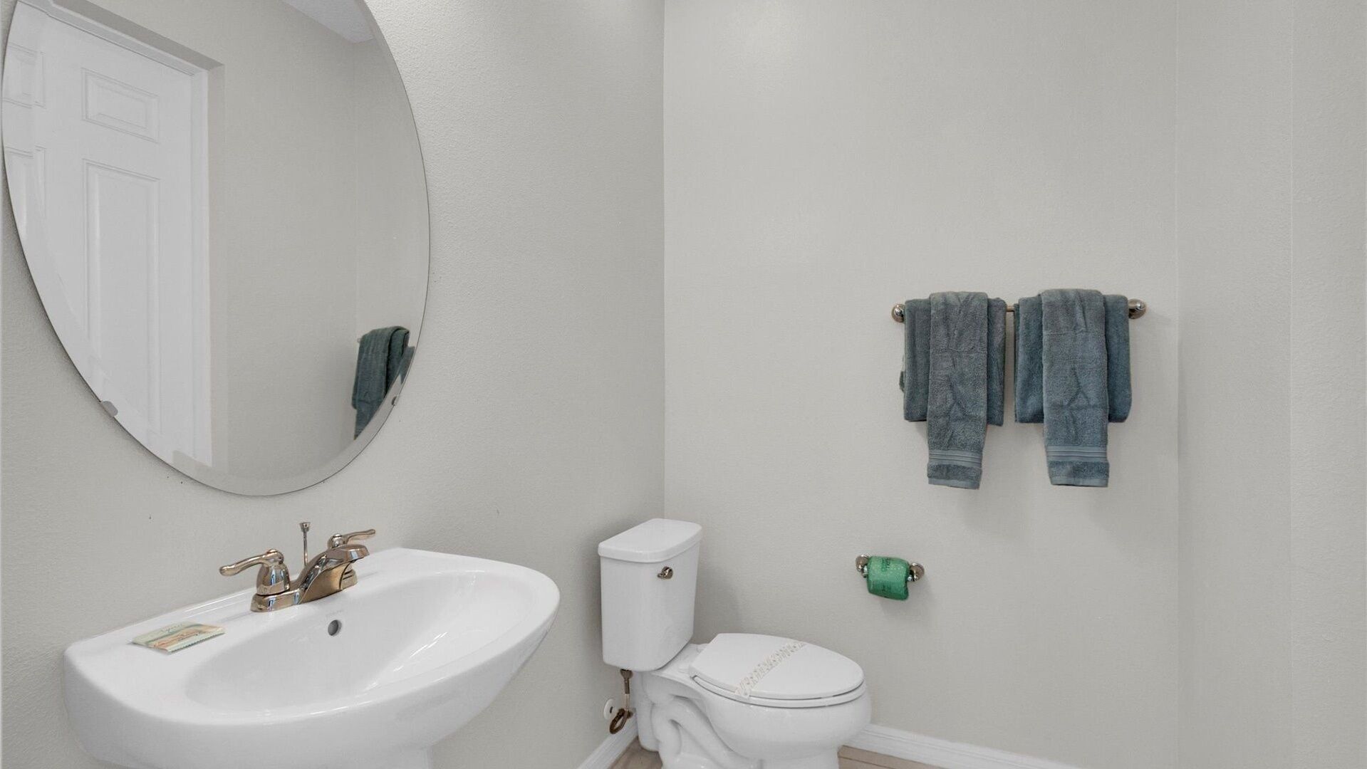 Un baño con lavamanos blanco, inodoro y espejo redondo.