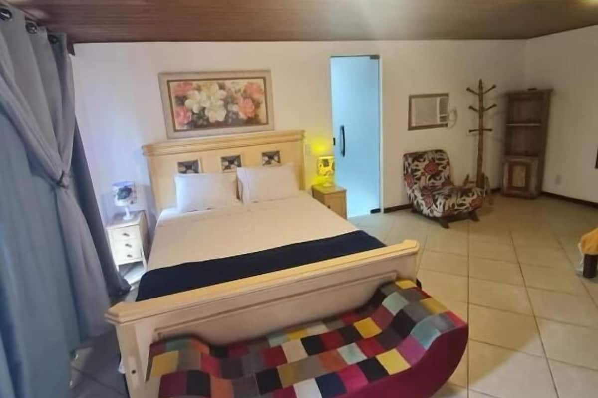 Un dormitorio con cama, banca, silla, armario y puerta.