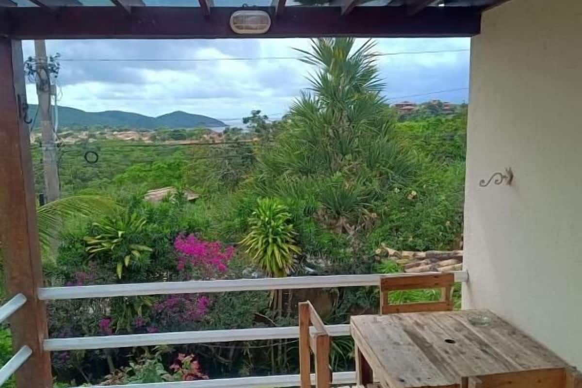 Un balcón con mesa y sillas de madera, con vistas a un jardín exuberante y colinas distantes.
