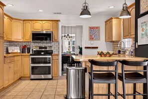 A modern kitchen with wooden cabinets, stainless steel appliances, and a central island with bar stools. - Stylish Ardsley Park Bungalow in Prime Location by Lucky Savannah (Savannah)