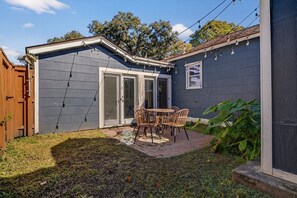 A backyard with a patio, a table and chairs, a wooden fence, and a large plant. - Stylish Ardsley Park Bungalow in Prime Location by Lucky Savannah (Savannah)