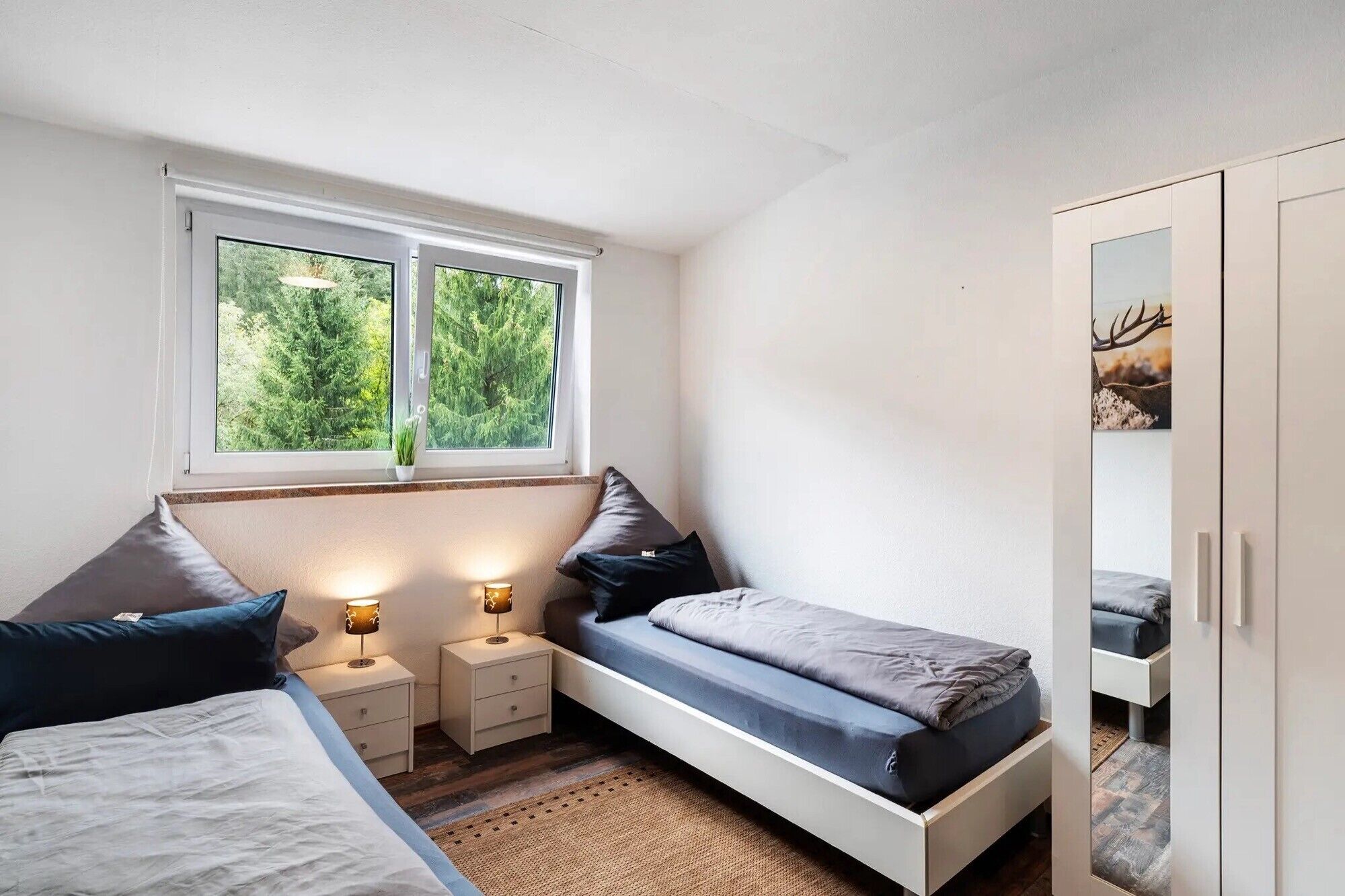 Een slaapkamer met een bed, nachtkastjes, een raam met uitzicht op bomen en een kledingkast.