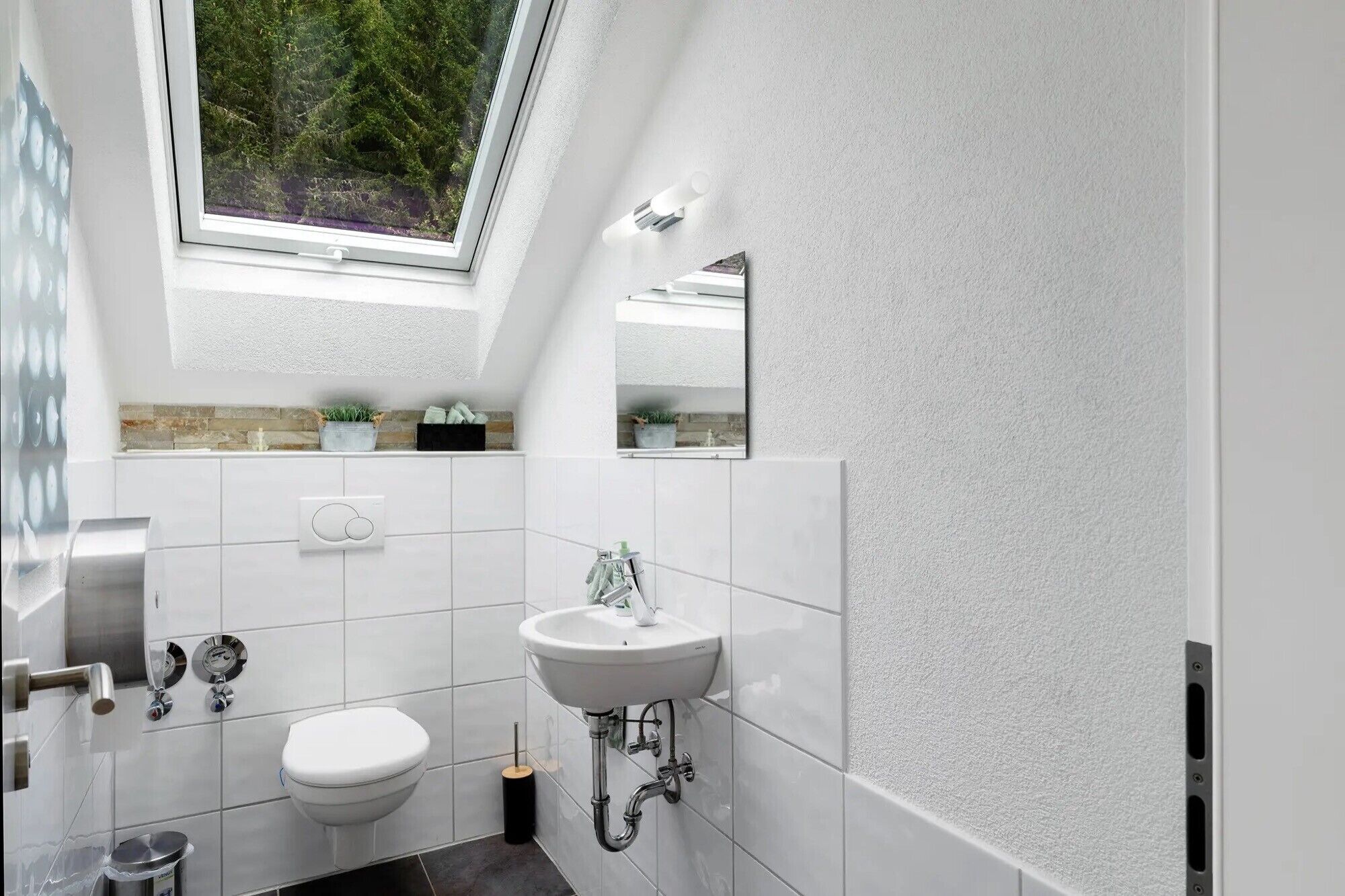 Une salle de bain moderne avec un puits de lumière, des carreaux blancs, des toilettes, un lavabo et une douche.