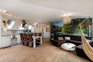A modern interior with a dining area, sofa, hammock, and a mural of a forest. - Apartment 'Villa Eichwald - Schwarzwaldloft' with Shared Garden, Balcony and Wi-Fi (Freudenstadt)