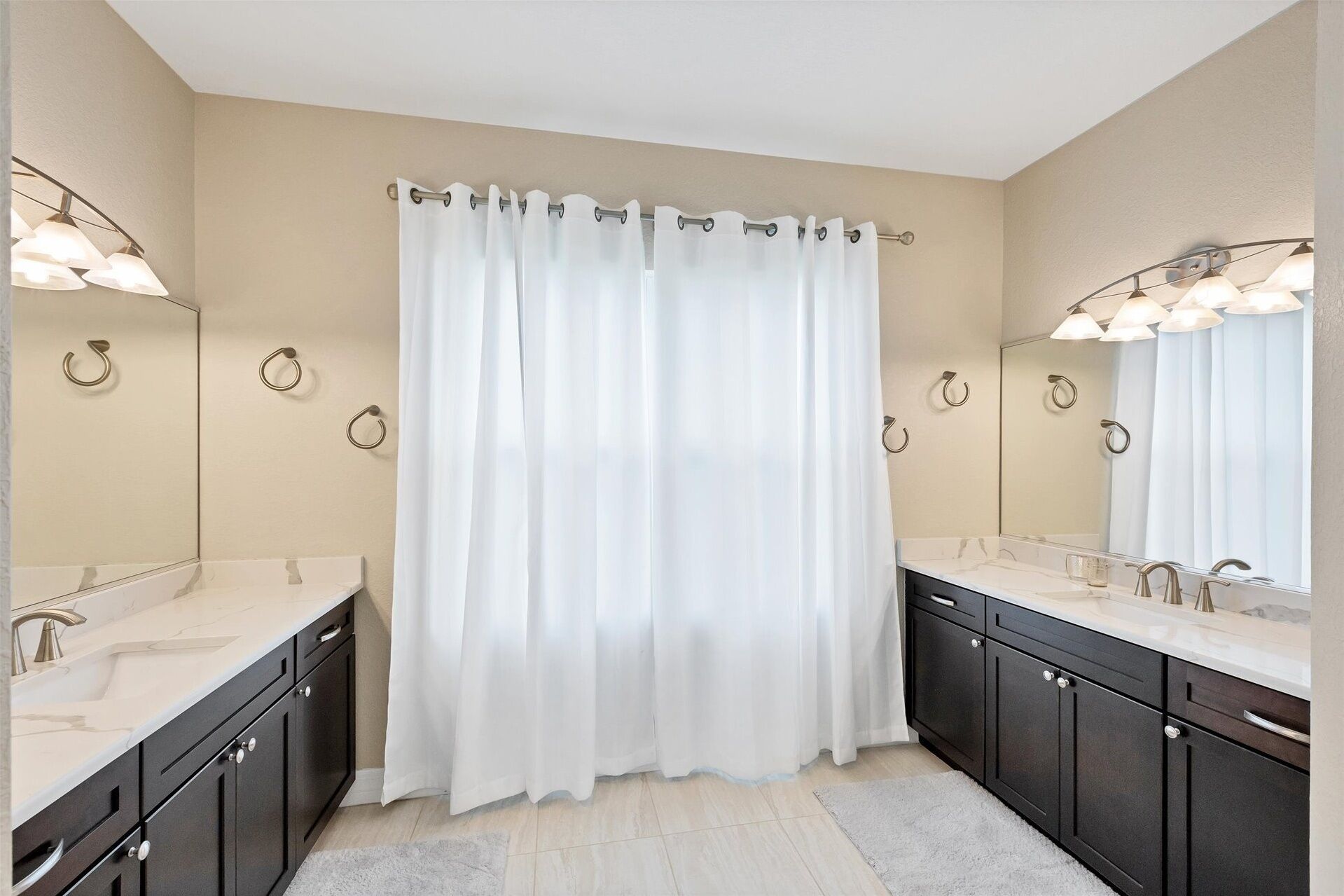 A bathroom with a white shower curtain, two sinks with mirrors, and wall-mounted towel rings.
