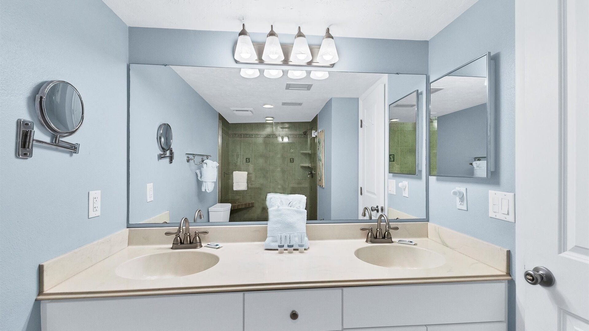 A bathroom with two sinks, a large mirror, and a shower visible in the background.