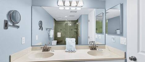 A bathroom with two sinks, a large mirror, and a shower visible in the background.