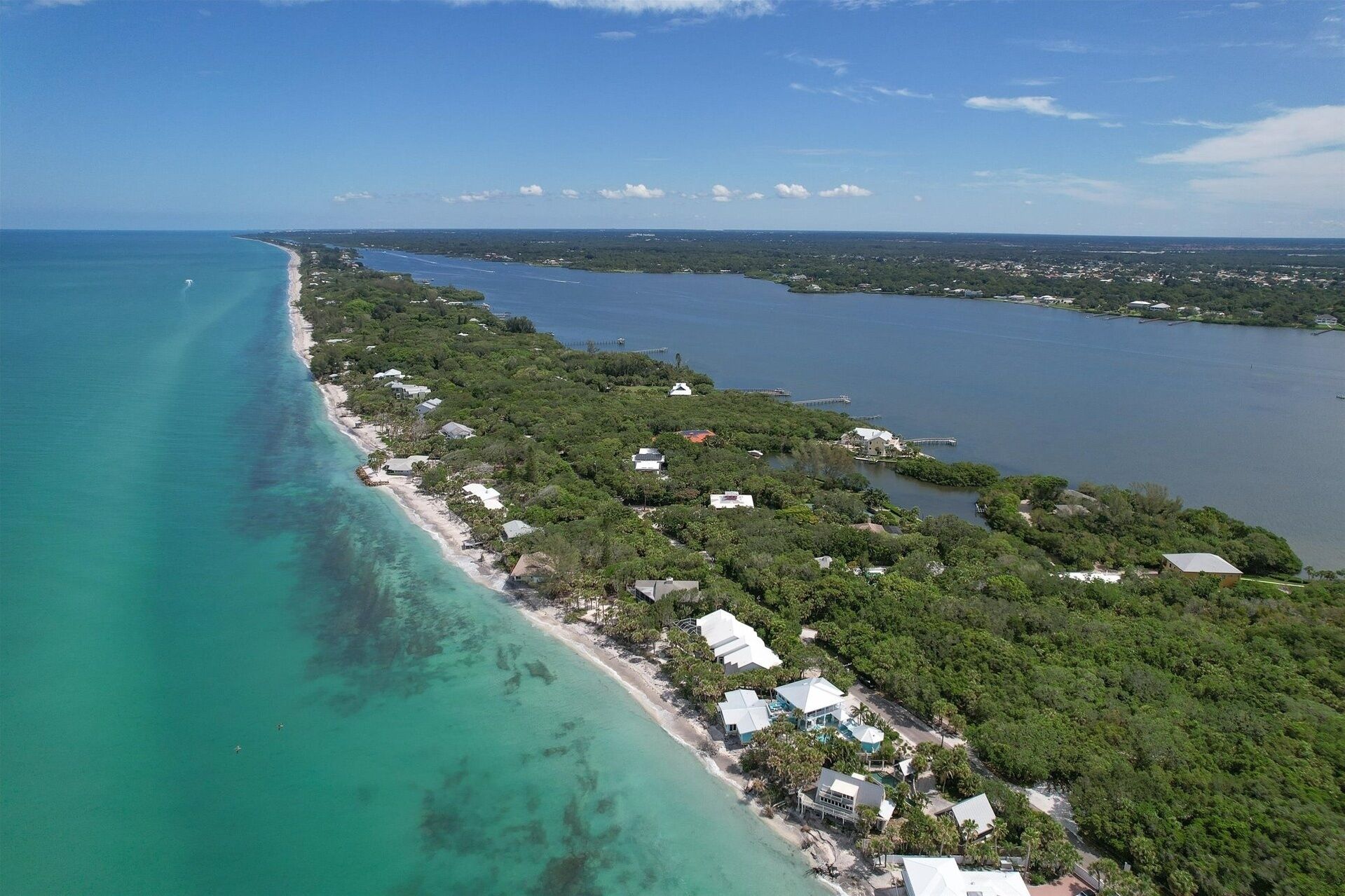 Vue aérienne d’une propriété côtière dotée d’une longue plage, d’une végétation luxuriante et d’une mer d’un bleu limpide.