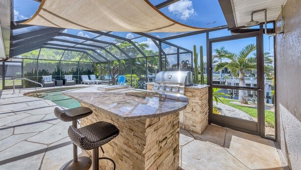 Ein überdachter Außenbereich mit Pool, Barhocker und Grill.