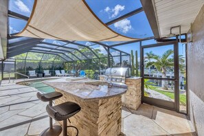 Un espace extérieur abrité comprenant une piscine, des tabourets de bar et un barbecue.