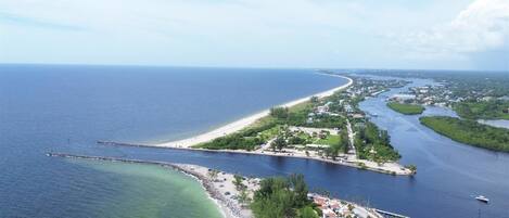 An aerial view of a coastal area with a beach, a marina, and a small island with buildings.