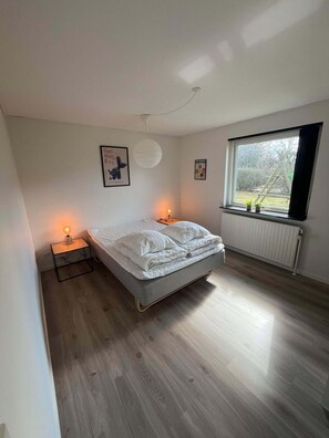 Une chambre à coucher avec un lit, des lampes de chevet, un radiateur et une fenêtre donnant sur l’extérieur.