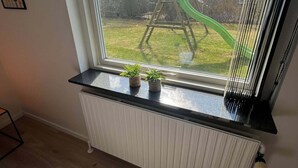 Une pièce dotée d’une grande fenêtre donnant sur un jardin avec une balançoire en bois et un toboggan vert.