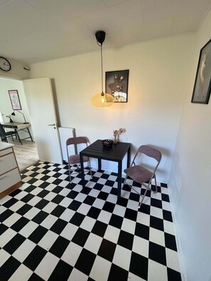 Une pièce avec un sol à carreaux noirs et blancs, une table entourée de chaises, un luminaire suspendu et un tableau encadré accroché au mur.