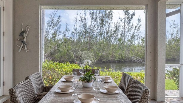 A dining area with a table set for six, overlooking a natural landscape with trees and a body of water. - Height Of Luxury In Bird Section Of Punta Gorda Isles 3 Bedroom Home (Punta Gorda)