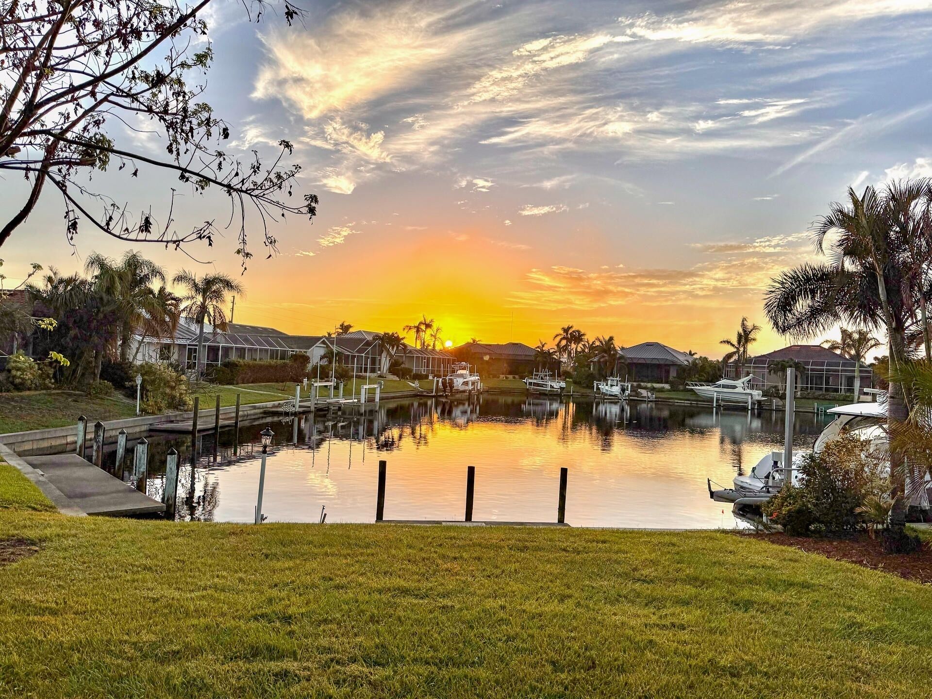 A marina with boats docked, surrounded by residential houses and palm trees, during sunset.