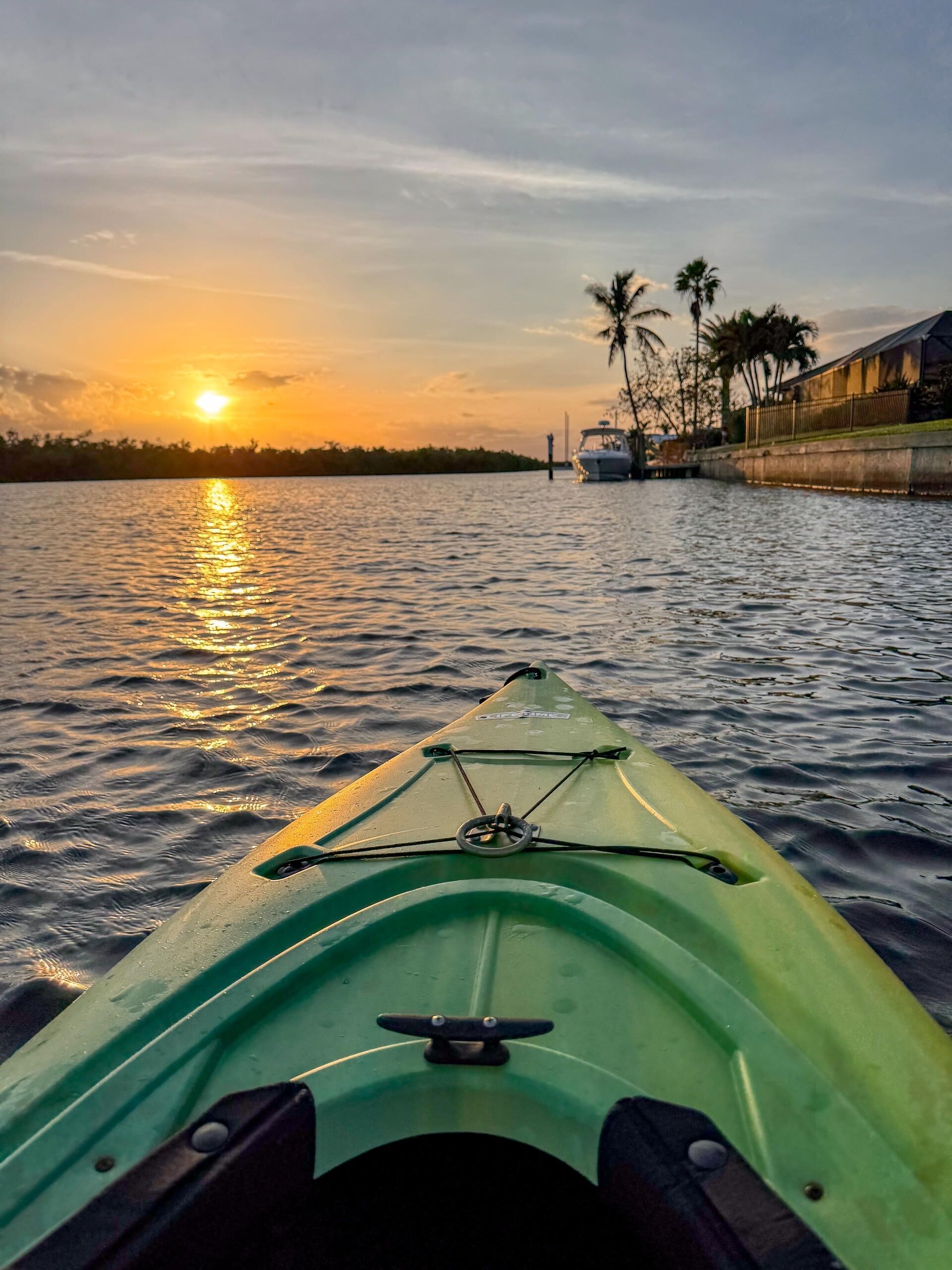 A green kayak on calm water with a sunset in the background.
