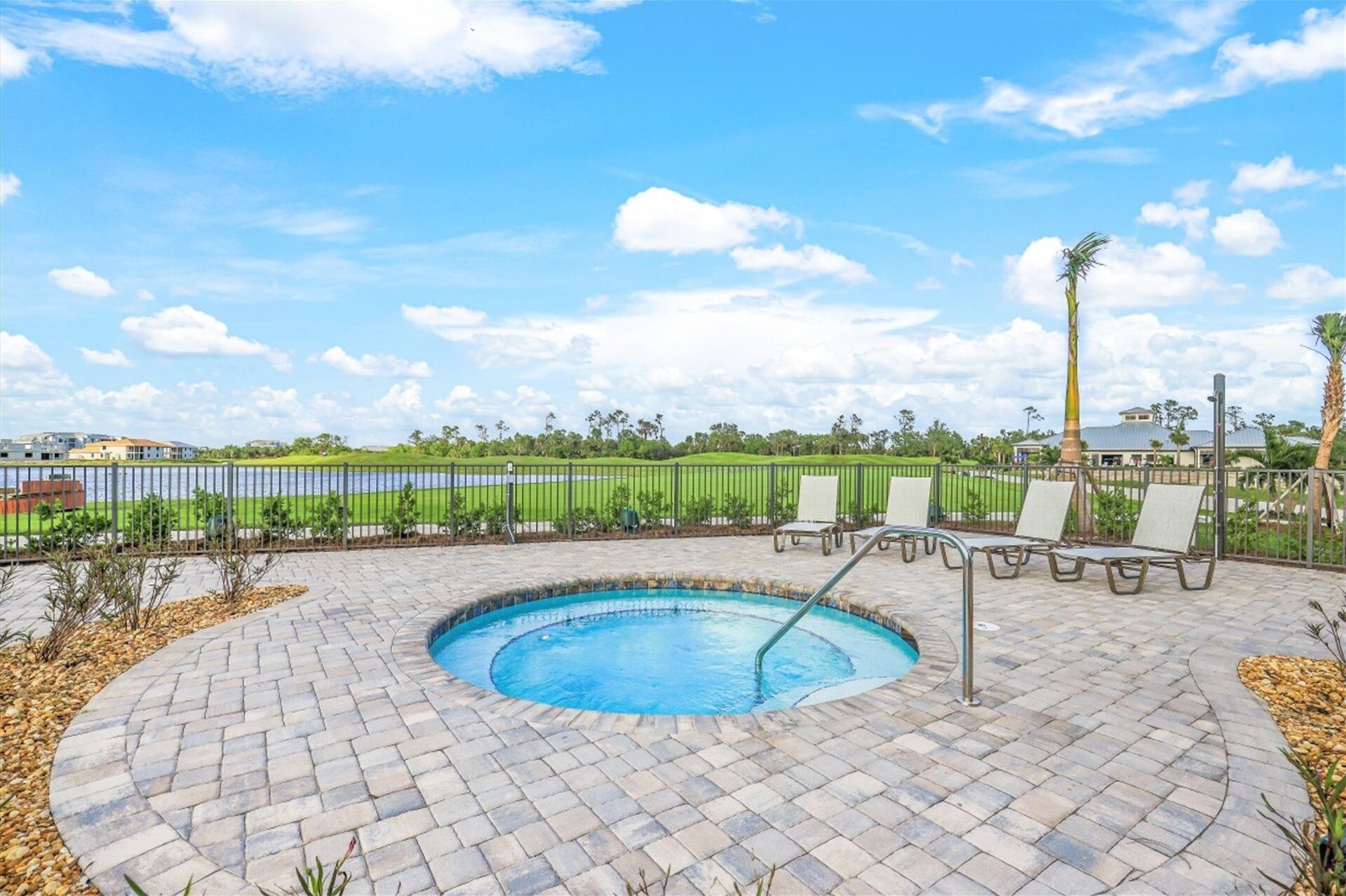 A swimming pool with a brick patio, lounge chairs, and a view of a golf course and buildings in the background.