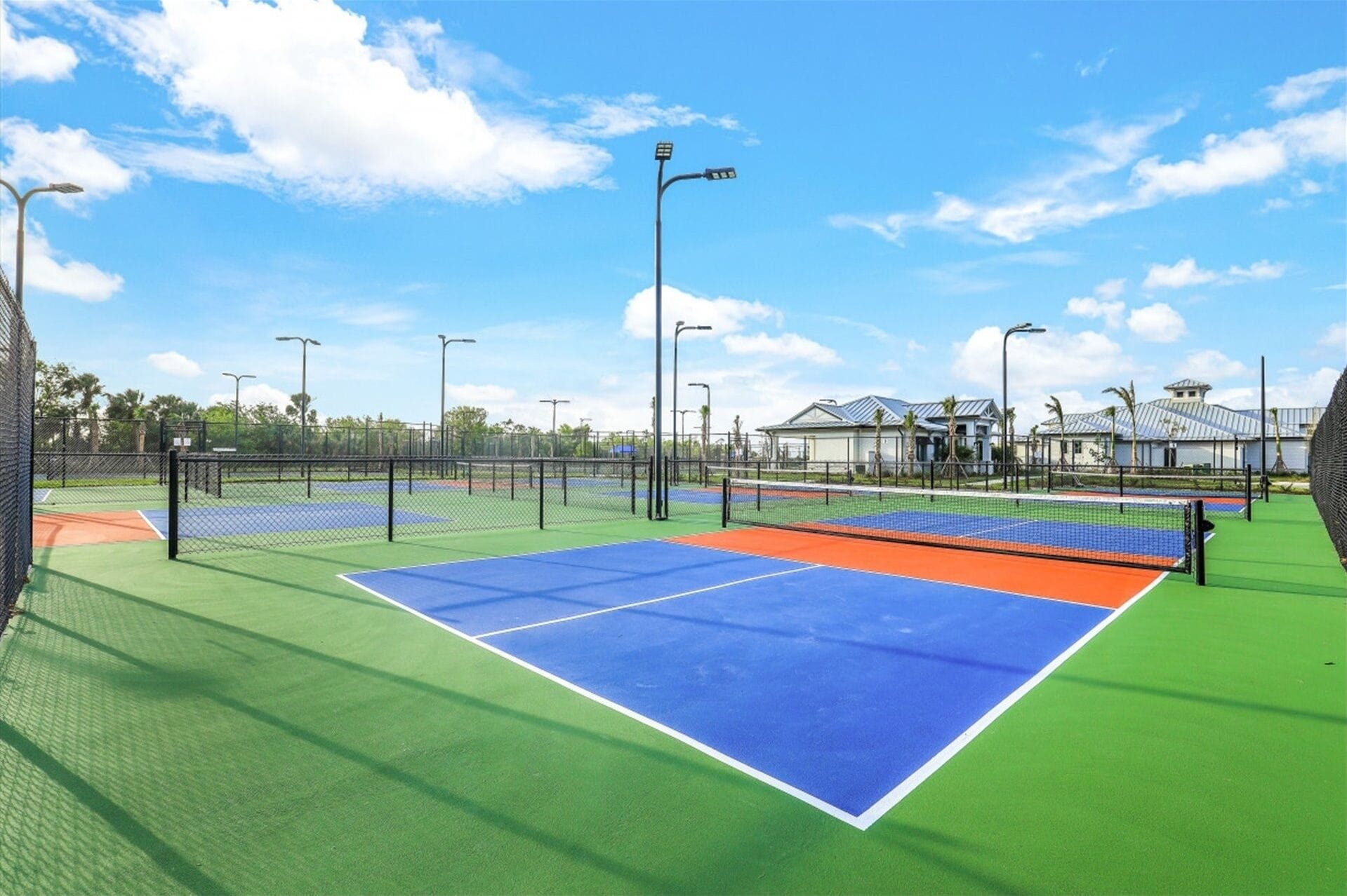 An outdoor tennis court with multiple courts, surrounded by a fence, and under clear skies.