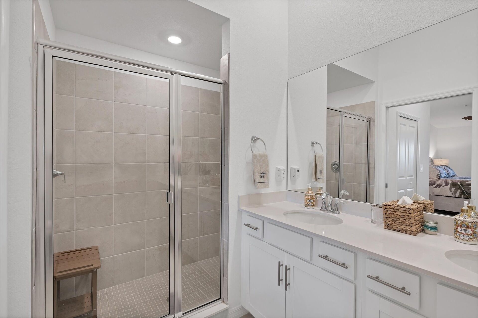 Un baño moderno con cabina de ducha de vidrio, muebles blancos y un espejo grande.
