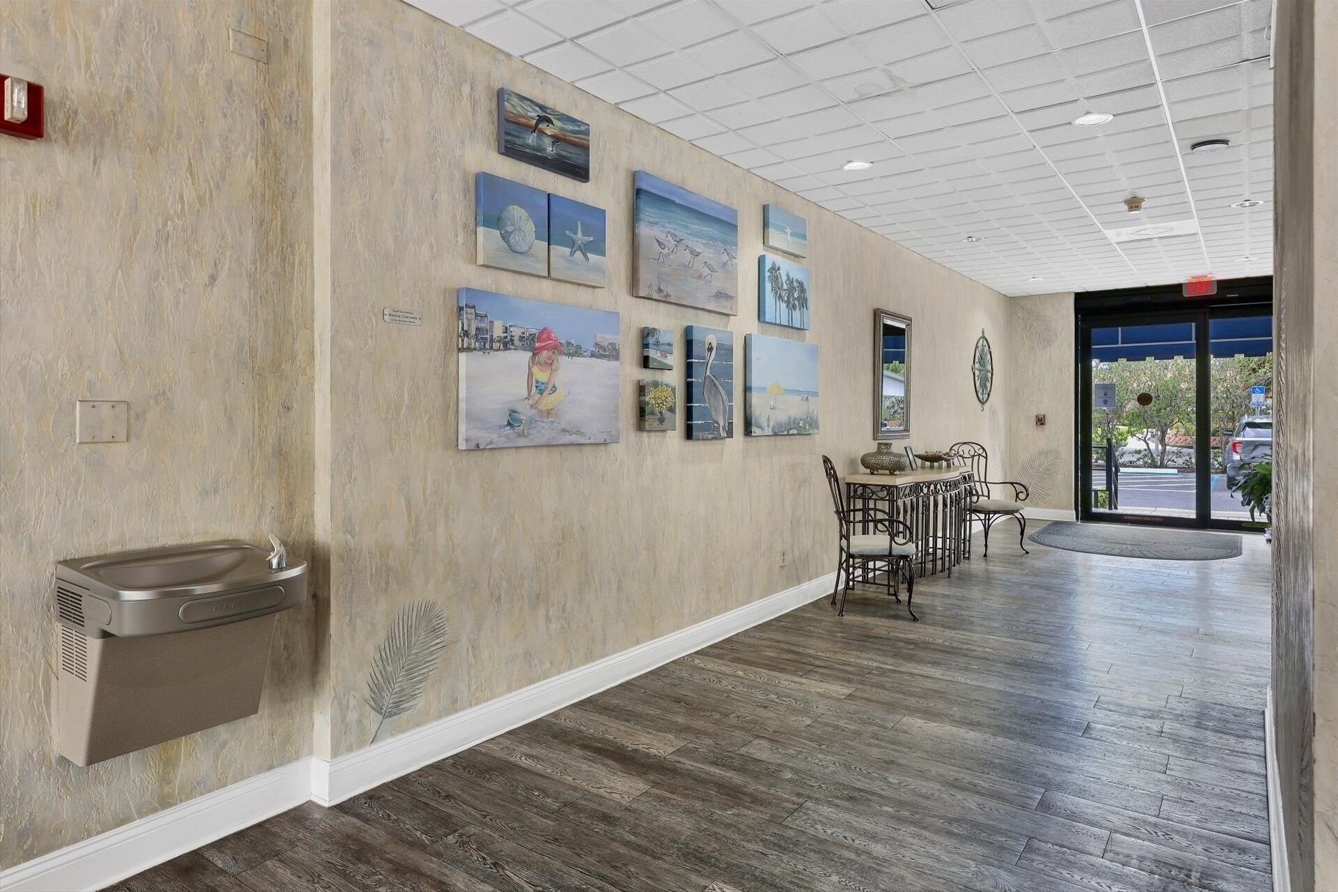 A hallway with a wooden floor, a reception desk, and several framed artworks on the wall.