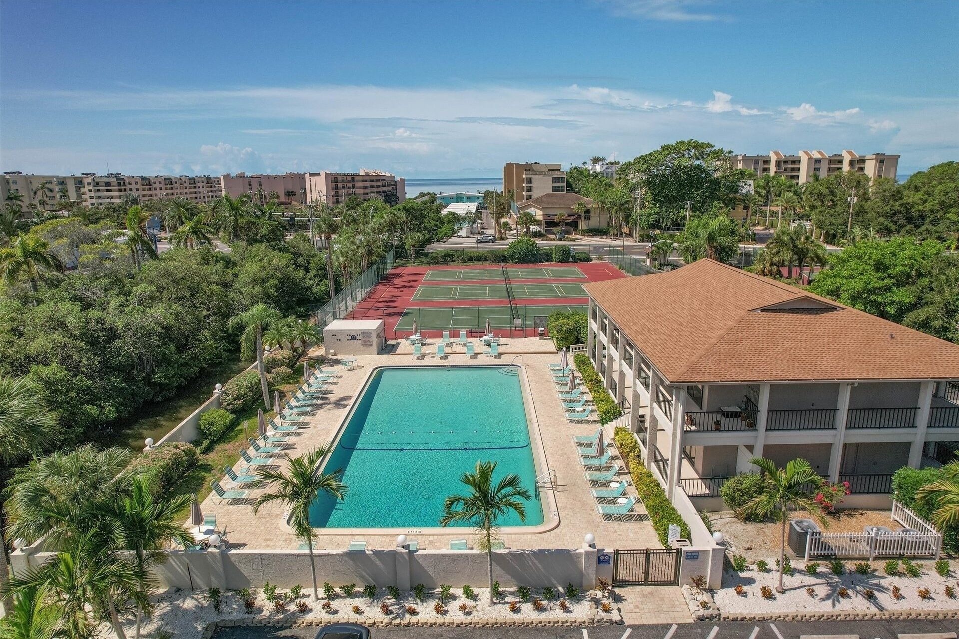 A resort with a central swimming pool, tennis courts, and a view of the ocean.