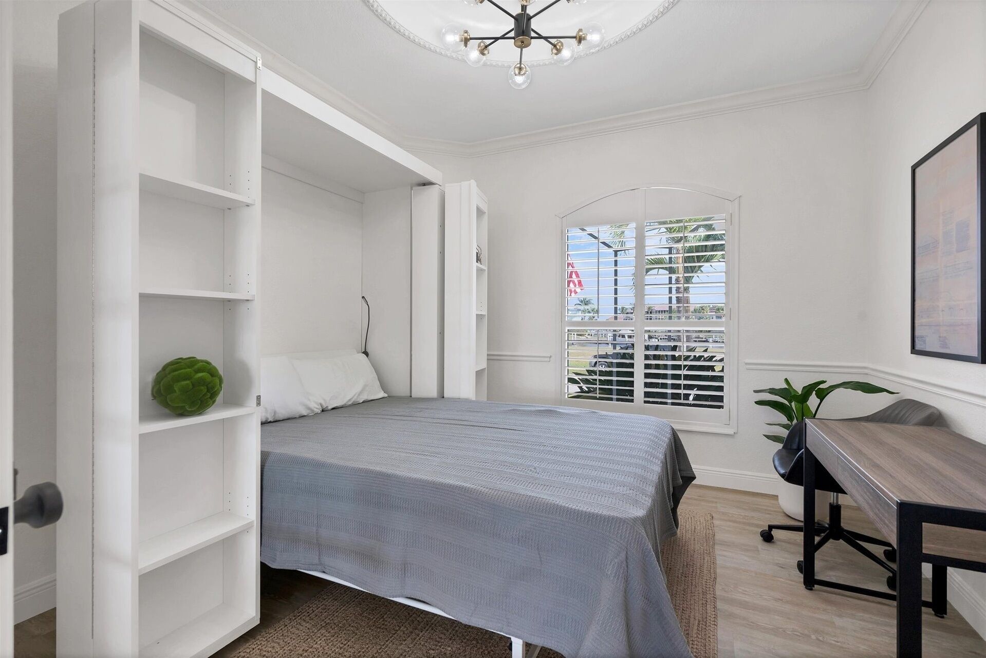 A bedroom with a bed, a desk, and a window with blinds.