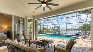 A sunlit patio with a pool, outdoor furniture, and a view of a lake and houses. - Punta Gorda Isles 4-Bedroom Private Pool Home on Canal 4 Home (Punta Gorda)