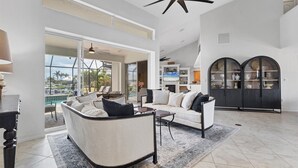 A spacious living room with a large sofa, a coffee table, and a fireplace. There is a balcony with a pool view. - Punta Gorda Isles 4-Bedroom Private Pool Home on Canal 4 Home (Punta Gorda)