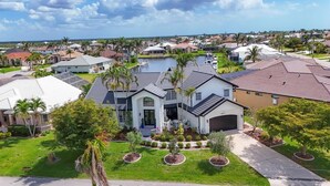 A large, modern house with a garage, surrounded by well-maintained lawns and palm trees. - Punta Gorda Isles 4-Bedroom Private Pool Home on Canal 4 Home (Punta Gorda)