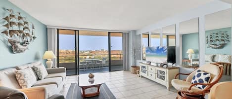 A spacious living room with a balcony, a television, and nautical-themed wall art.