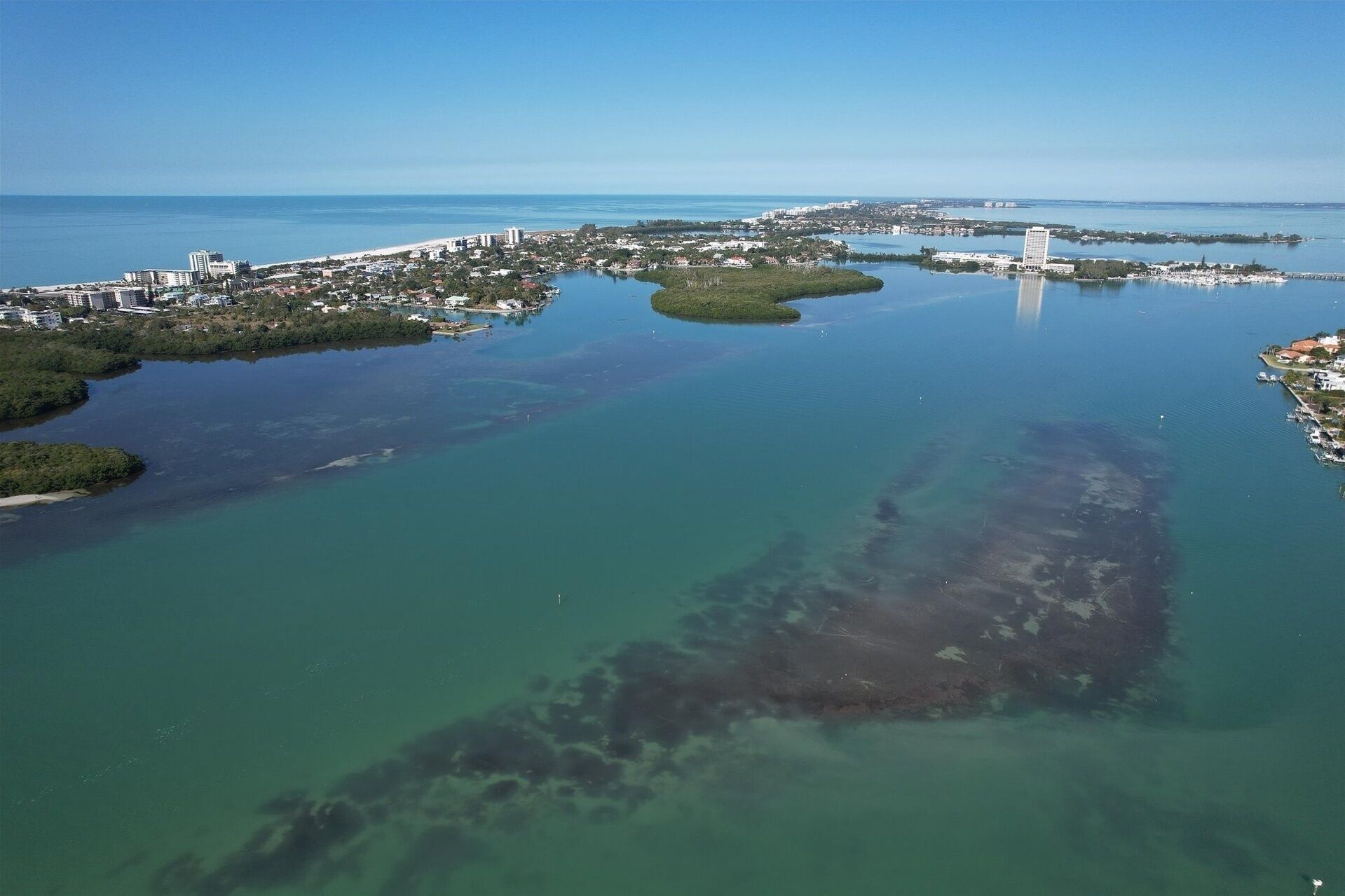 Une vue aérienne d’une ville côtière, avec une vaste étendue d’eau, plusieurs îles et un pont imposant.