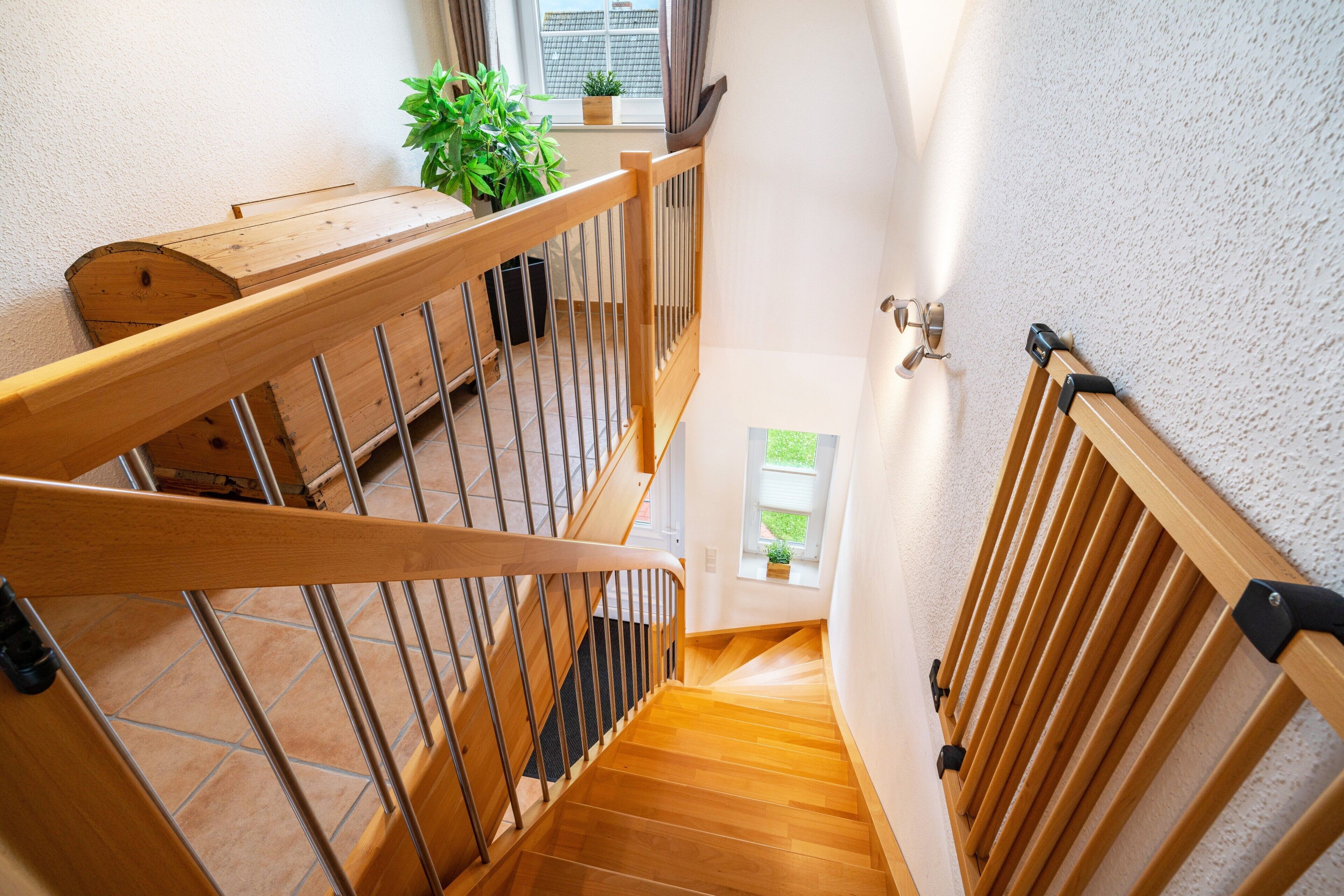 Eine Holztreppe mit Metallgeländern, ein kleines Fenster mit Pflanze und eine Tür mit Griff.