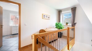Ein Zimmer mit einem hölzernen Bett, einem Topfpflanzen, einem gerahmten Bild und einem Fenster mit Vorhängen.