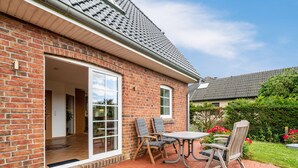 Ein Backsteinhaus mit Terrasse, einer Schiebetür und einem Tisch mit Stühlen.