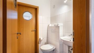 Un bagno piccolo e moderno con una porta in legno, uno specchio rotondo, un water, un lavandino e un porta asciugamani.
