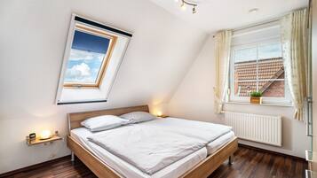 Une chambre à coucher avec un lit, une fenêtre avec des rideaux, un puits de lumière, une table de chevet avec une lampe et un radiateur.