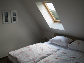 A bedroom with a skylight, a bed with floral bedding, and two framed pictures on the wall.