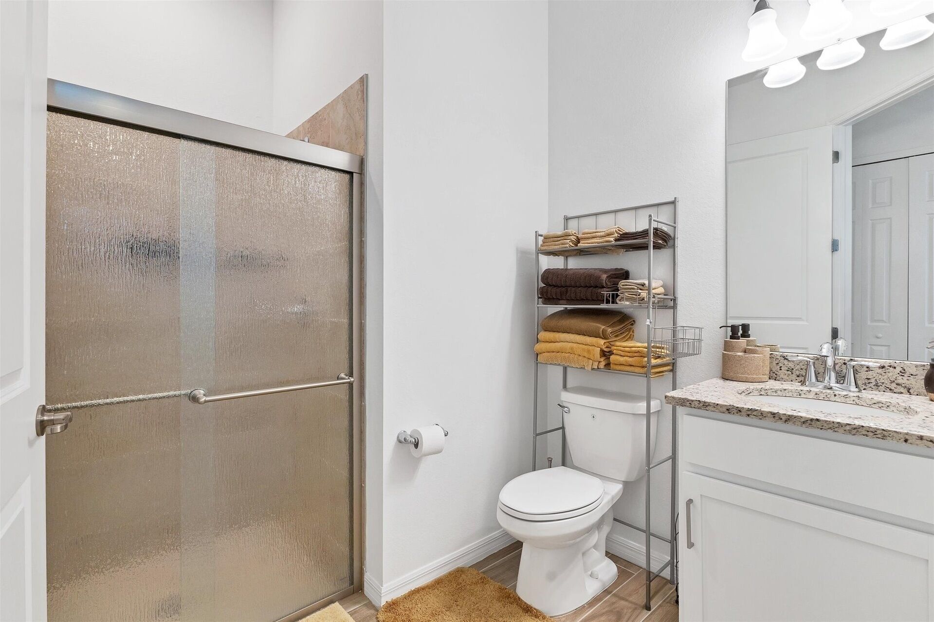 A bathroom with a toilet, a sink with a mirror, a towel rack, and a shower door.