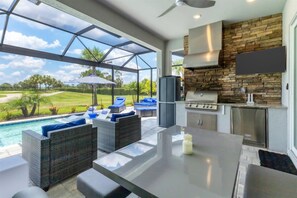 A modern outdoor kitchen with a stone backsplash, a large TV, and a poolside seating area with wicker furniture. - Private Pool Home With Golf Course View Heritage Landing Golf Resort - 30 Night Minimum 3 Bedroom Home (Punta Gorda)