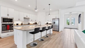A modern kitchen with white cabinetry, stainless steel appliances, a central island with bar stools, and a wooden floor. - Private Pool Home With Golf Course View Heritage Landing Golf Resort - 30 Night Minimum 3 Bedroom Home (Punta Gorda)