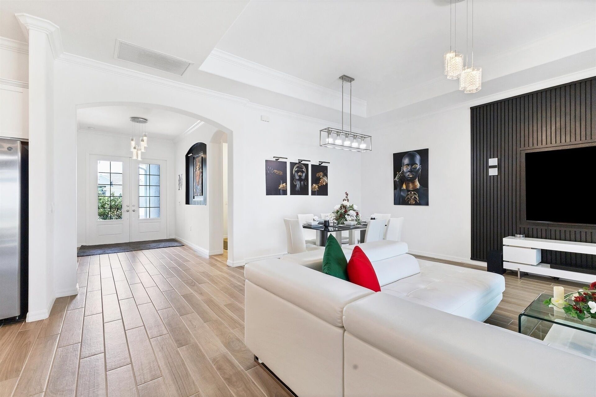 A modern living room with a white sofa, a dining area with a table and chairs, and a TV on the right.