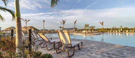 Un espace aménagé au bord de la piscine, avec des chaises longues, des palmiers et un ciel dégagé.